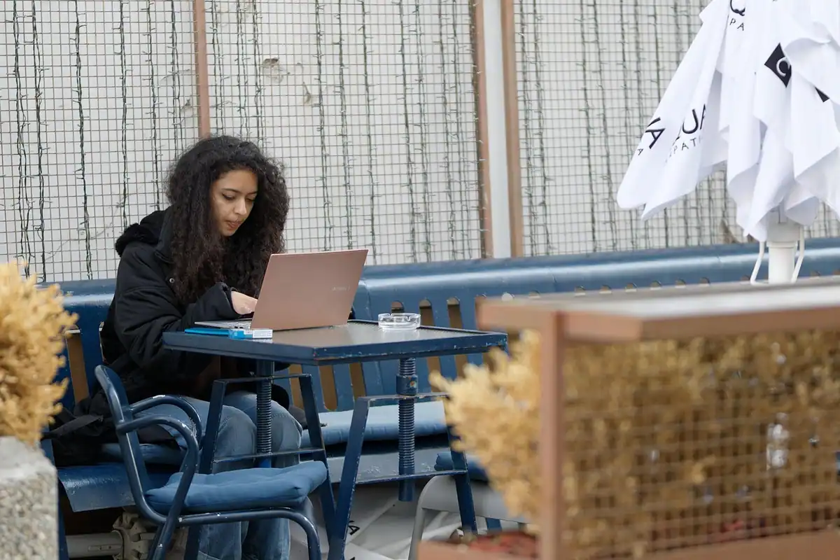 O fondatoare lucrează concentrată la laptop, la o masă de terasă, cu fonduri puține