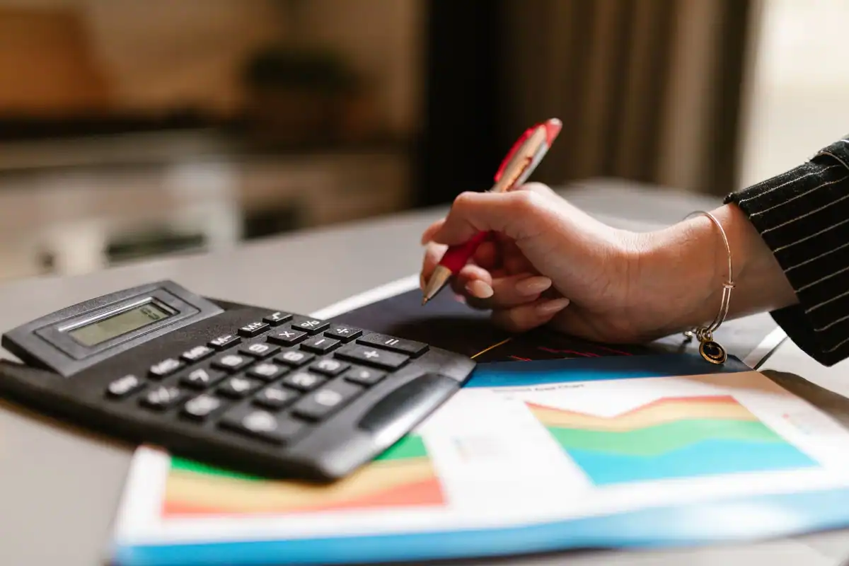 Un calculator și o mână cu pix roșu deasupra unor grafice colorate despre acționariat