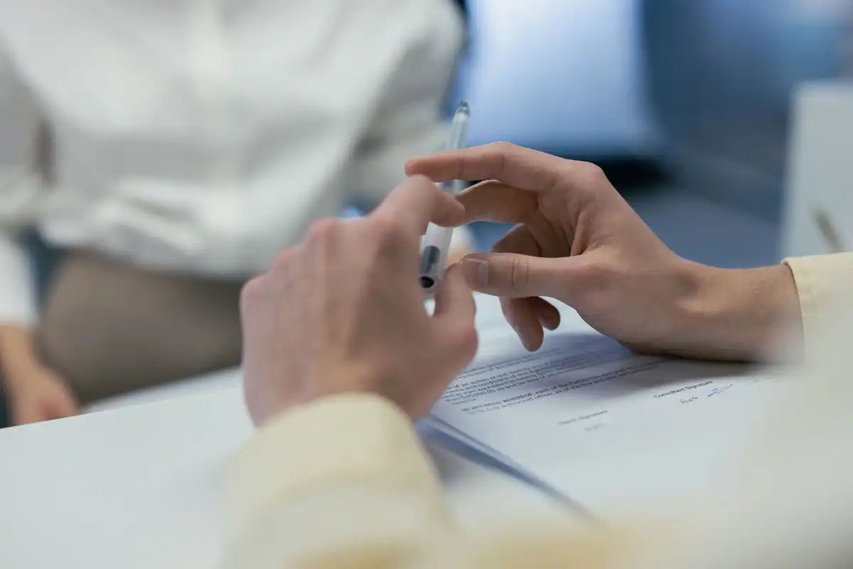 Două mâini țin un pix deasupra unui contract, în timpul semnării cu un furnizor extern
