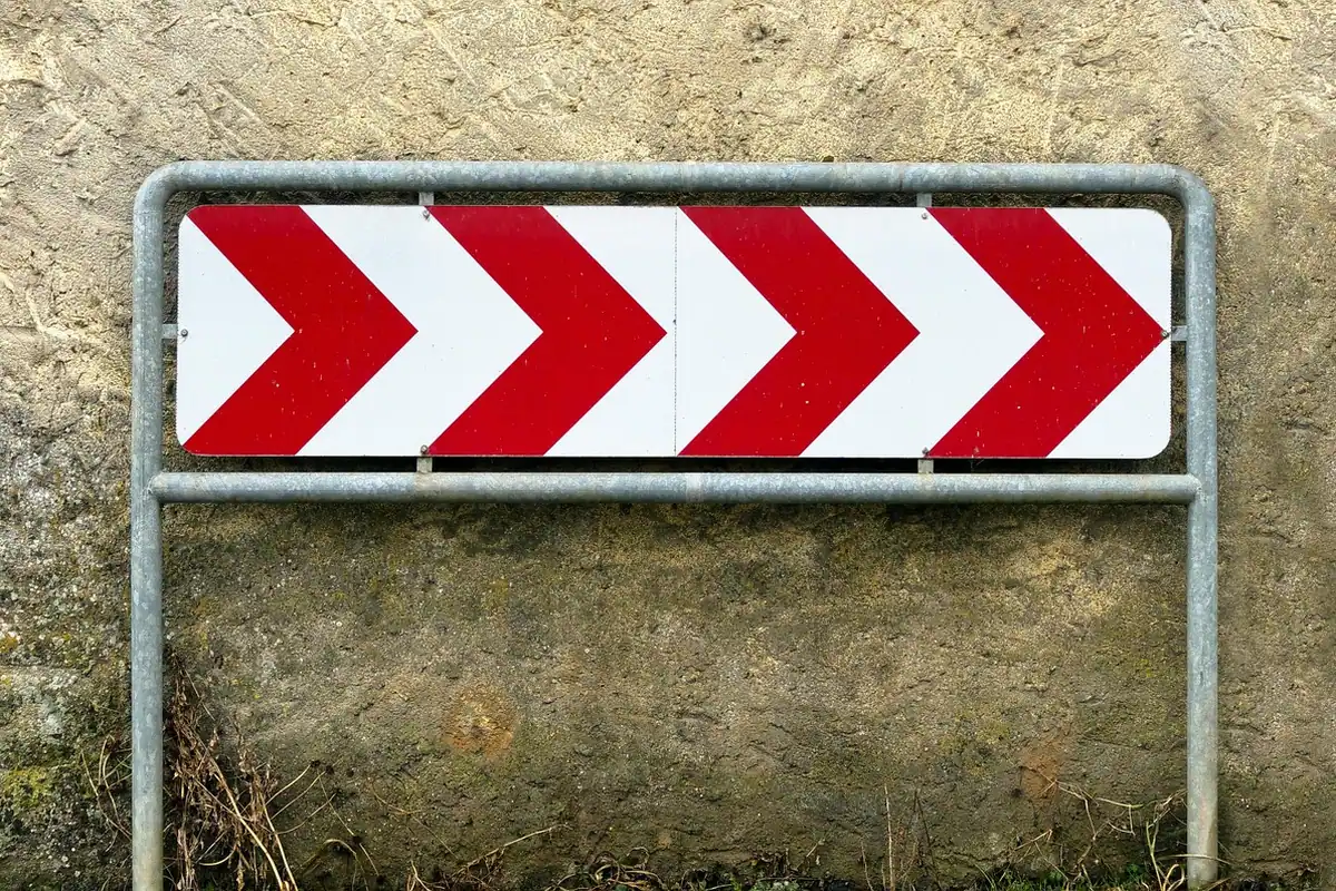 Un indicator rutier cu săgeți roșii și albe avertizează asupra unei curbe periculoase