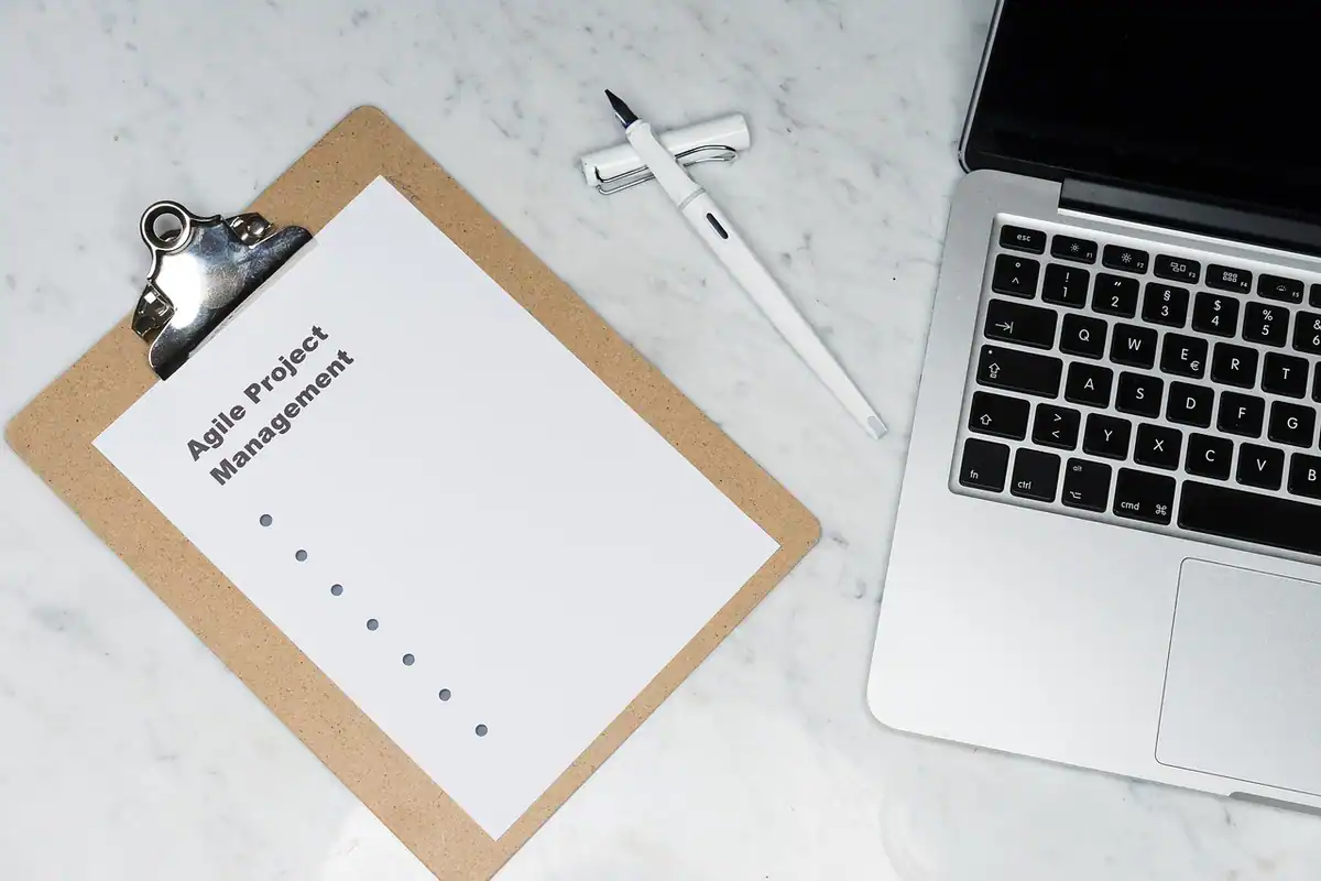 Un clipboard cu lista metodei agile lângă un laptop, pentru planul de lansare