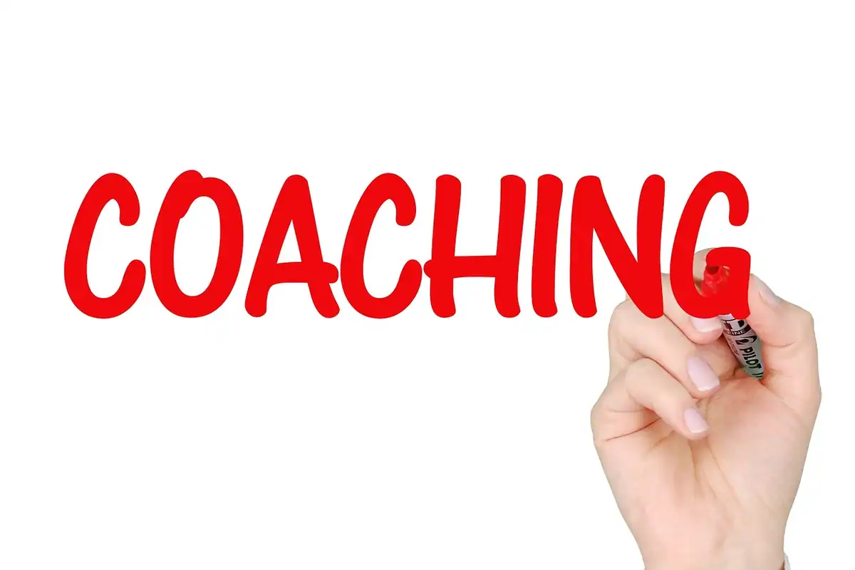 O mână scrie cu marker roșu cuvântul coaching, pe un fundal alb