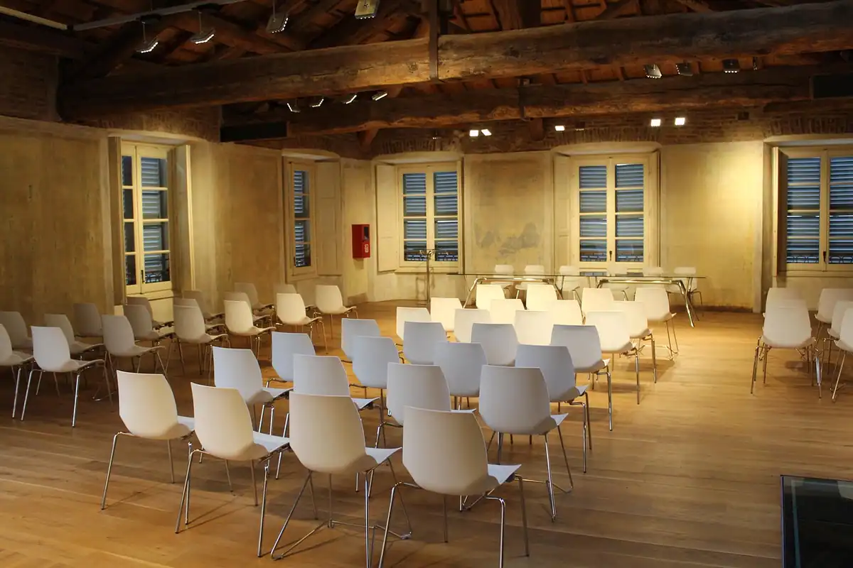 O sală de seminar goală, cu scaune albe aranjate în rânduri și lumină caldă