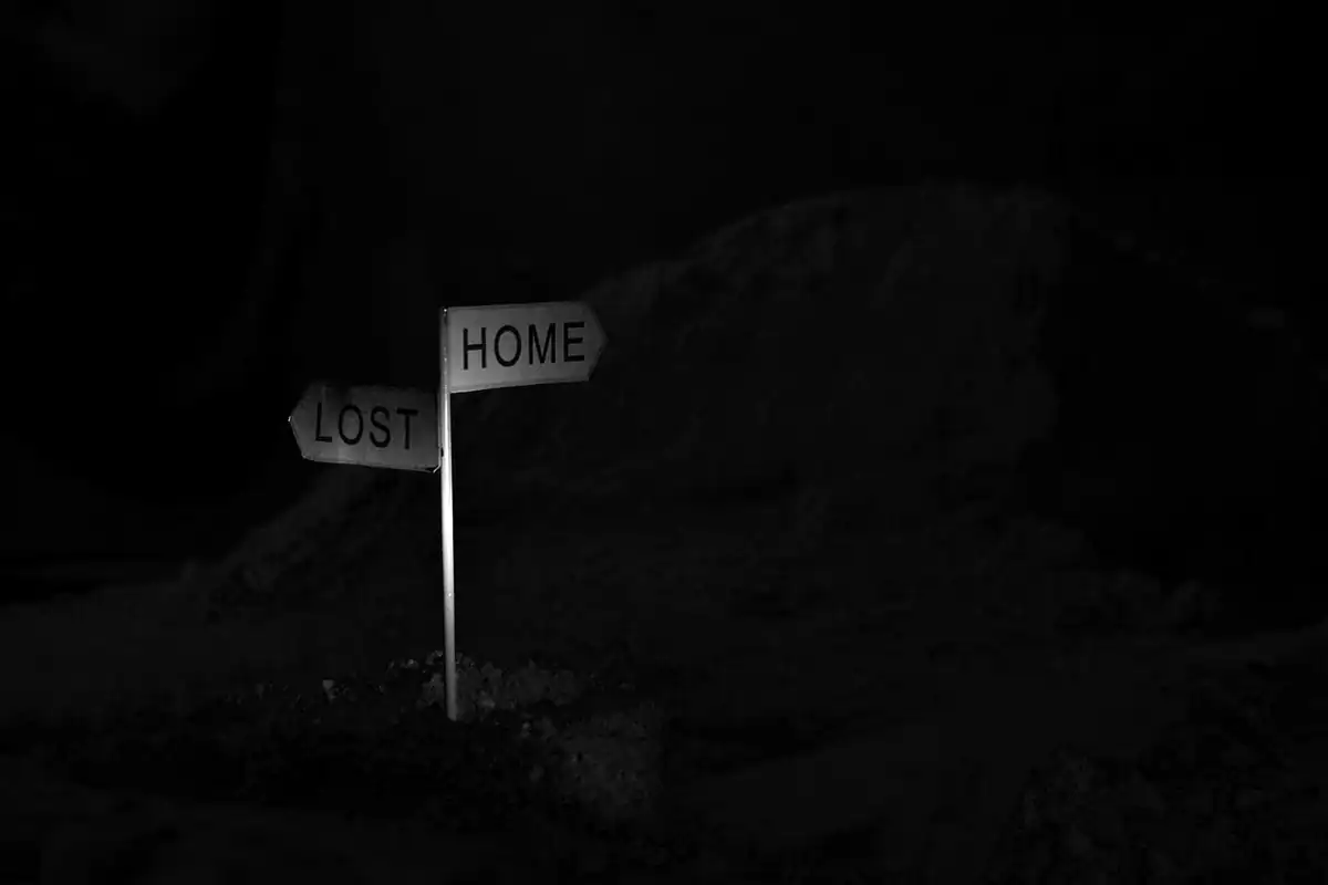 Un indicator cu două săgeți, spre acasă și spre pierdut, luminat noaptea într-un loc întunecat