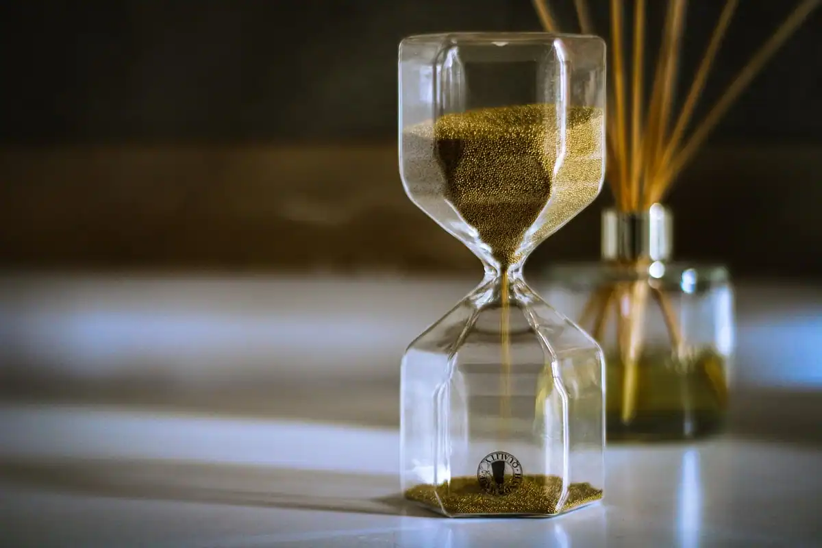 O clepsidră cu nisip auriu, lângă un flacon de parfum, arată trecerea timpului